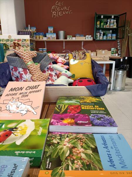 Gardening books, cushions and decorative items offered at Les Fleurs Bleues.”