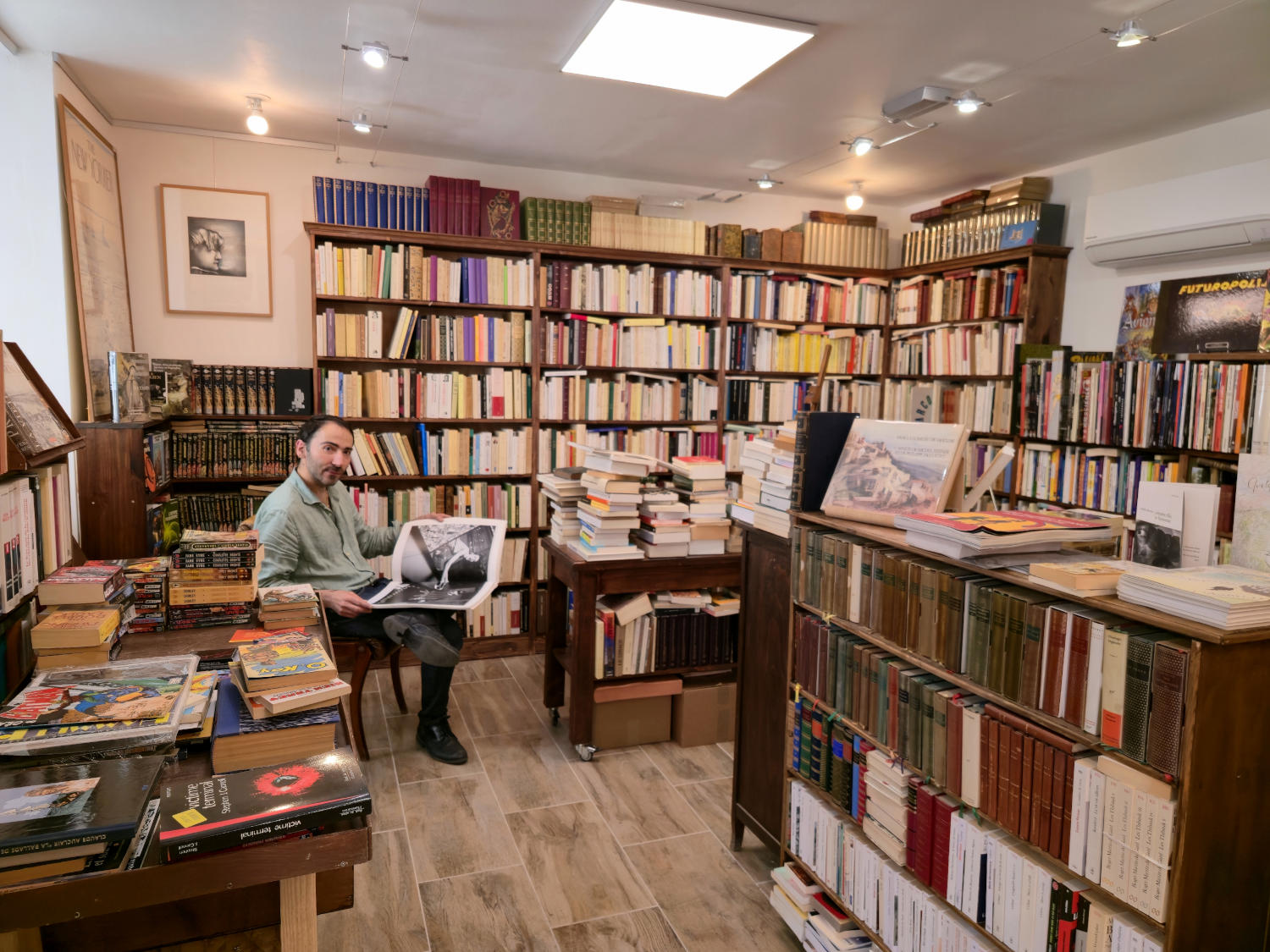 A bearded man is sitting in a well-stocked bookstore, surrounded by