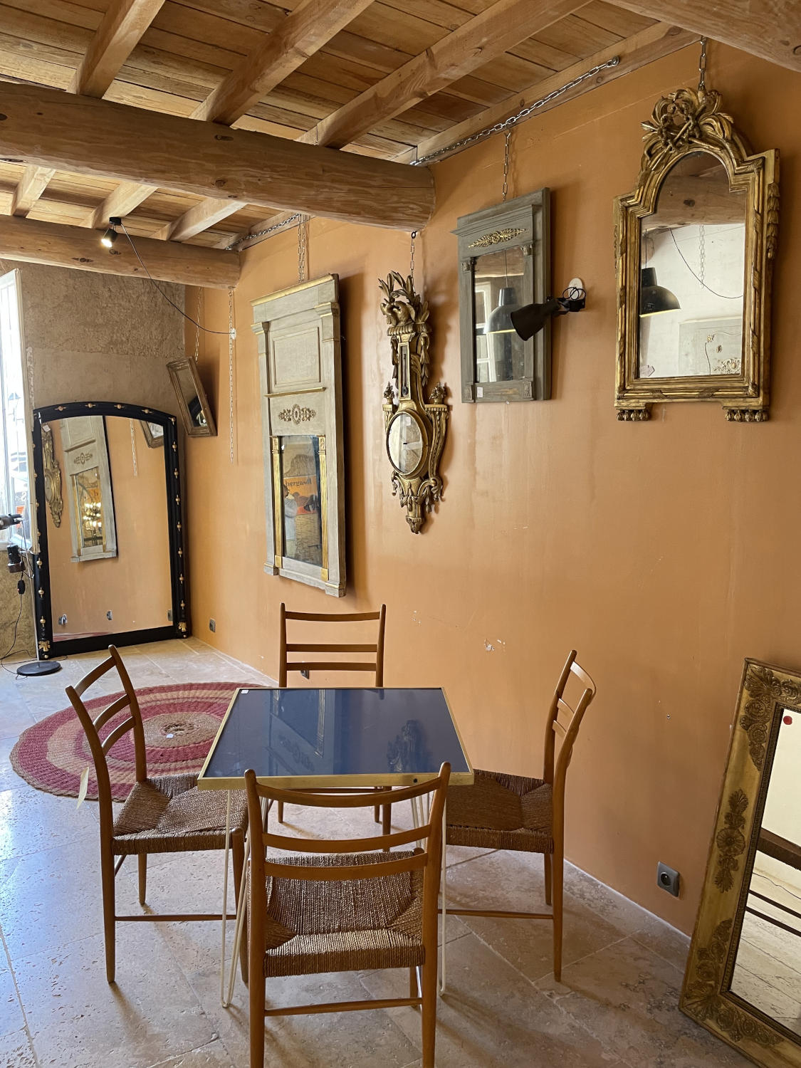 Warm living room in vintage style, with exposed stone walls, wooden armchairs, collection of mirrors and soft lighting.