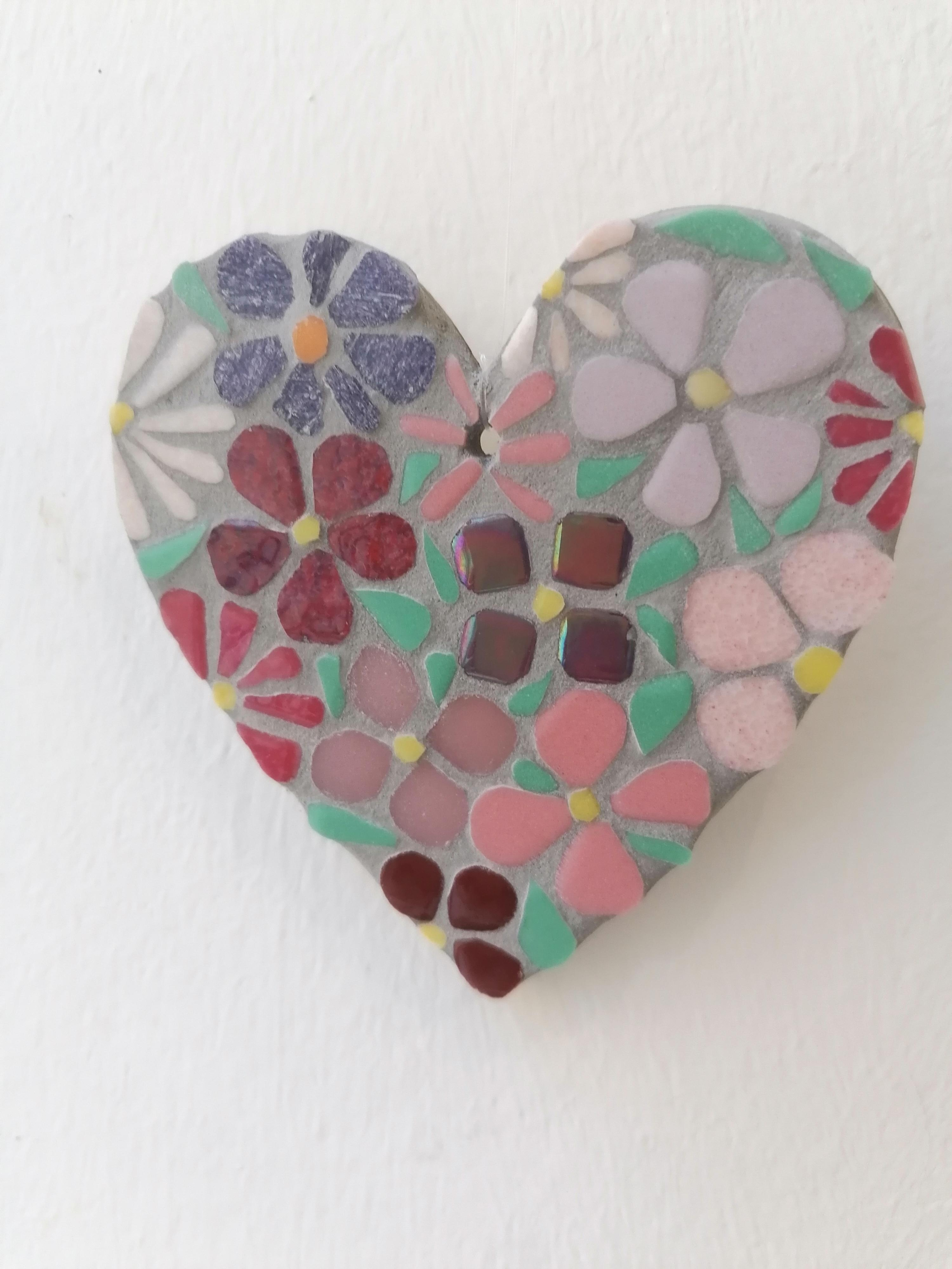 A heart-shaped ornament made from a mosaic of flowers and tiles. The dominant colors are pink, purple, burgundy, and blue-green.