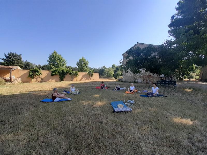 A group of women are sitting on yoga mats in a large field of