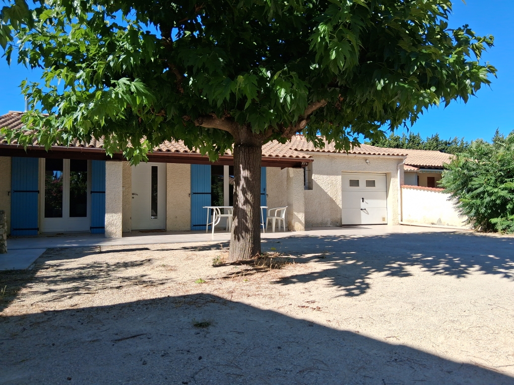 A one-story Provençal house, with blue shutters and a white garage, under a large leafy tree offering views