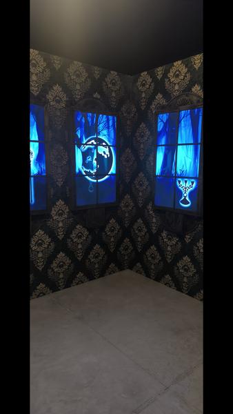 A dark room with black and gold damask wallpaper, and blue dummy windows, and blue illuminated dummy windows, displaying neon symbols such as a chalice and a full moon. 