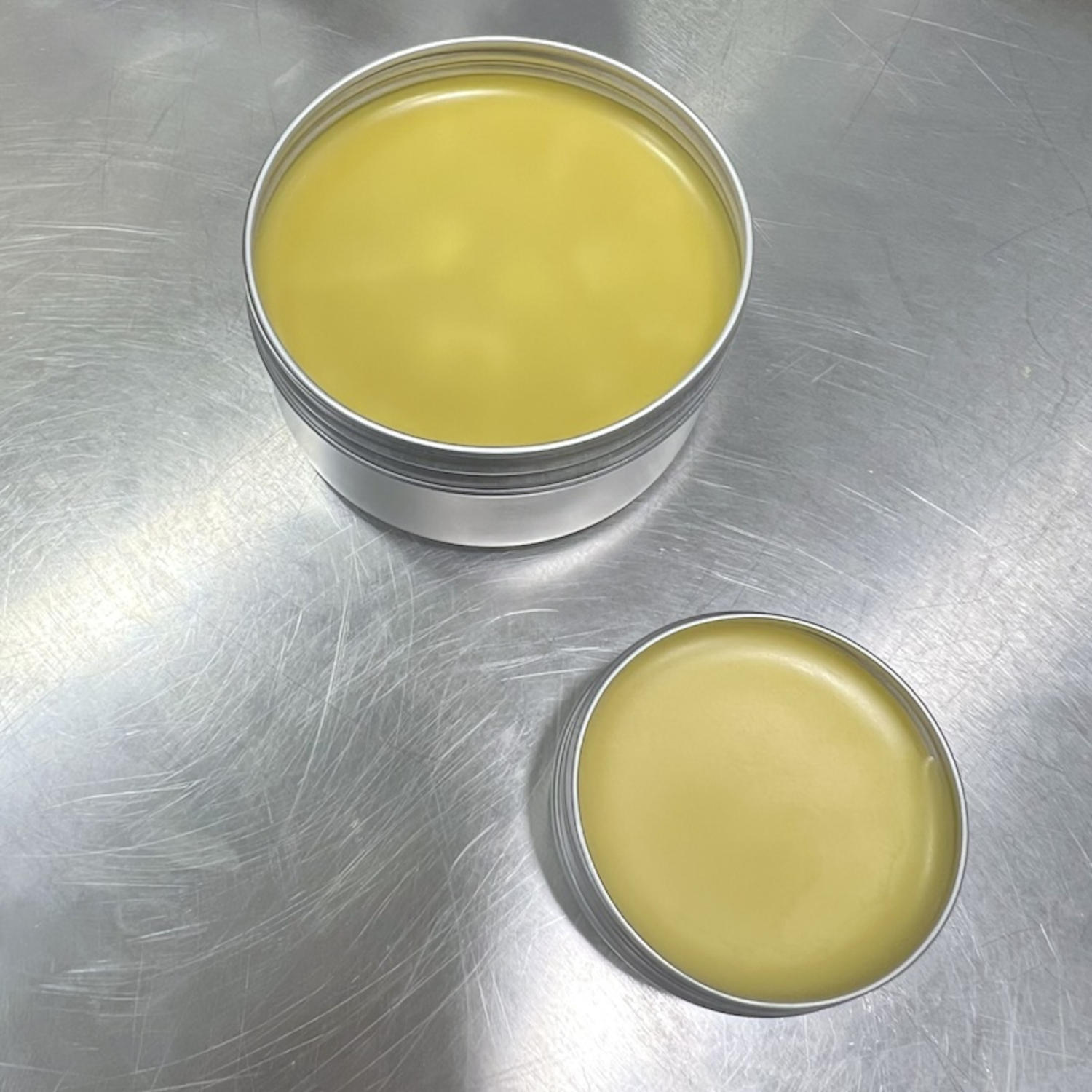 Two small metal boxes opened with a balm or a pale yellow cream.