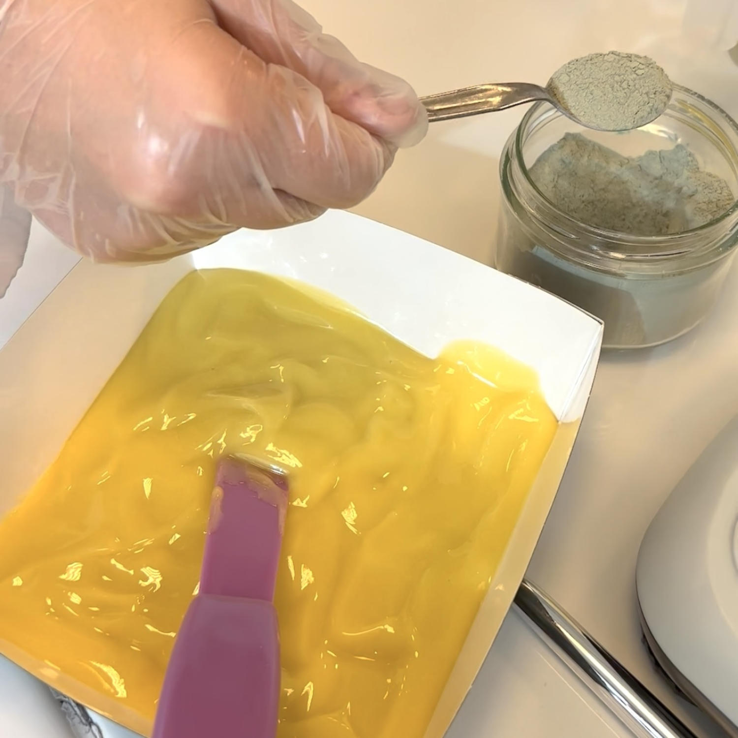 A gloved person pours a grey-green powder of