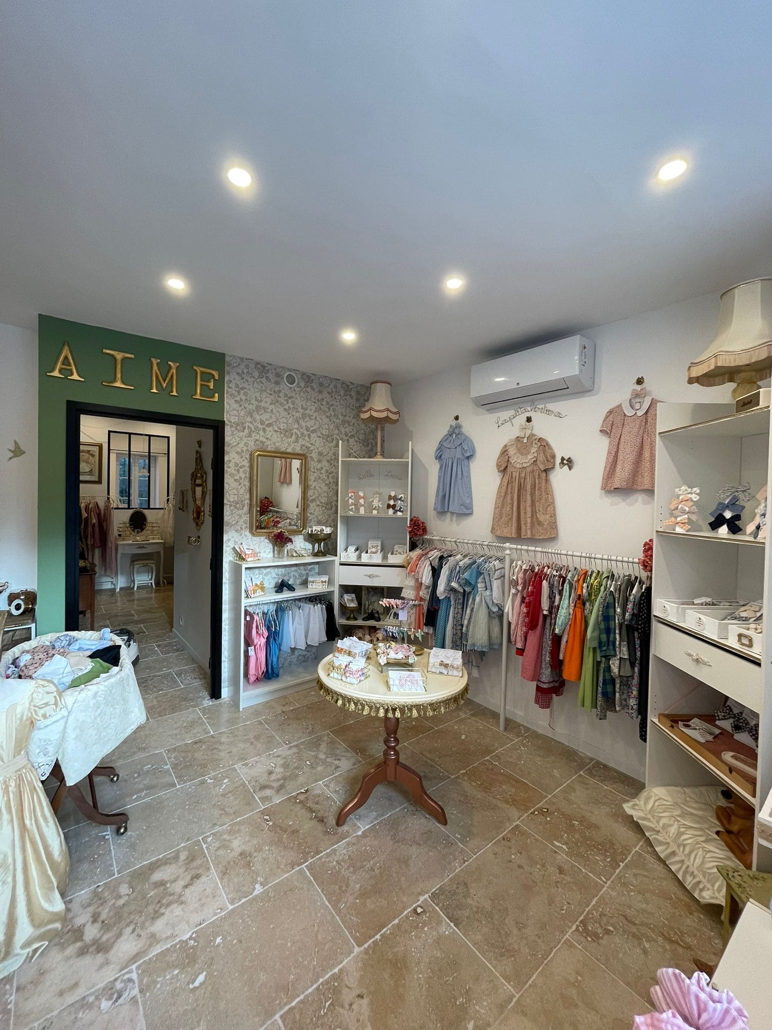 A bright boutique space with a light stone floor and decorated white walls. Several children