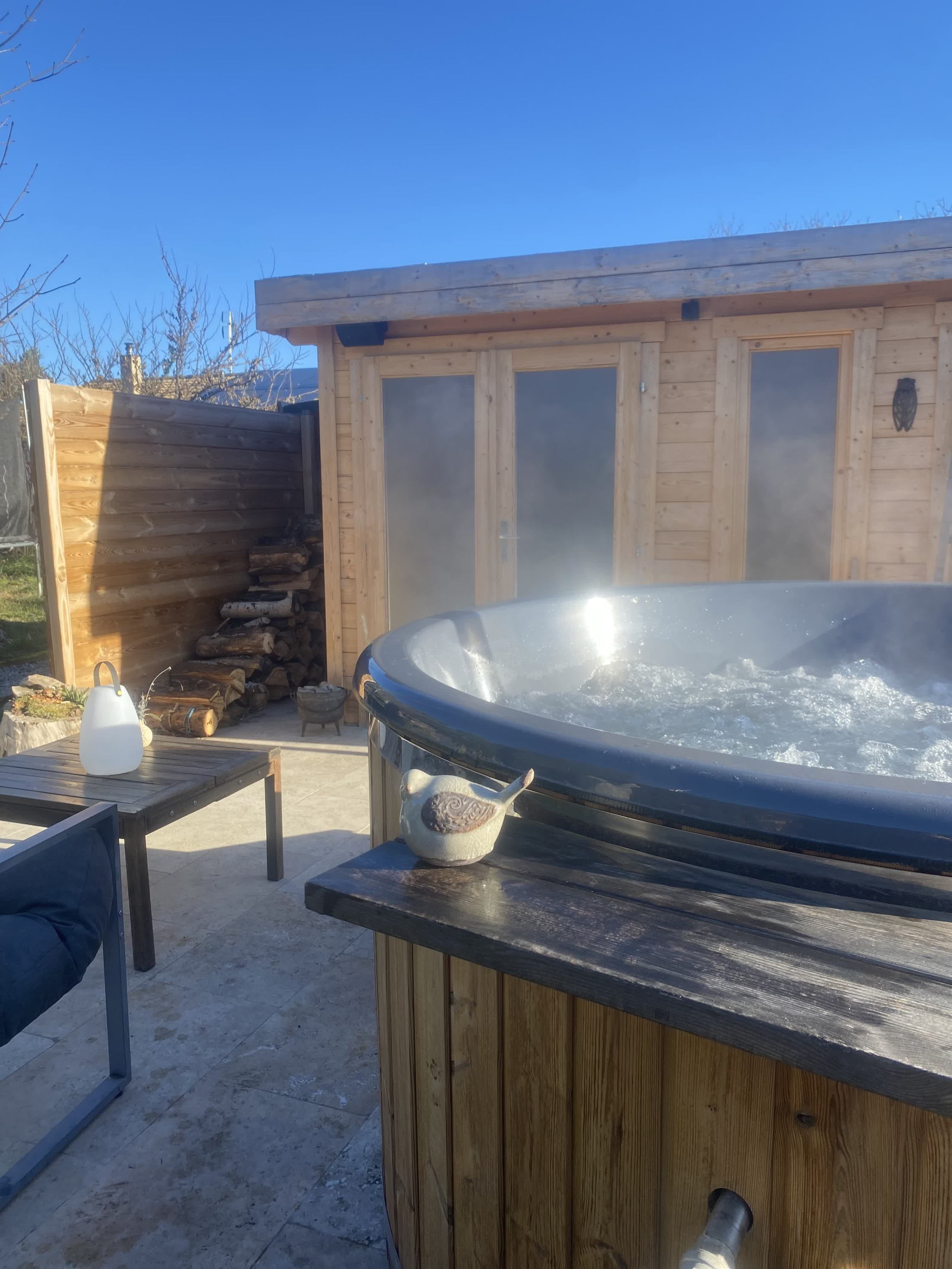 Outdoor wooden Nordic bath, heated and smoking, installed on a sunny terrace in front of a wooden chalet.