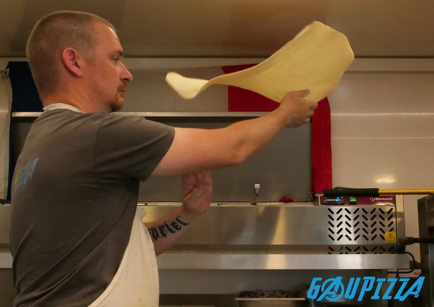A pizza chef stretches pizza dough in full motion, in a professional kitchen.