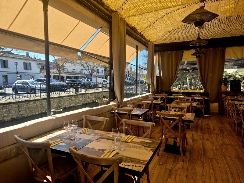 A restaurant terrace bathed in light, with wooden tables and a view of the dock. The atmosphere is warm and ideal for an outdoor meal.