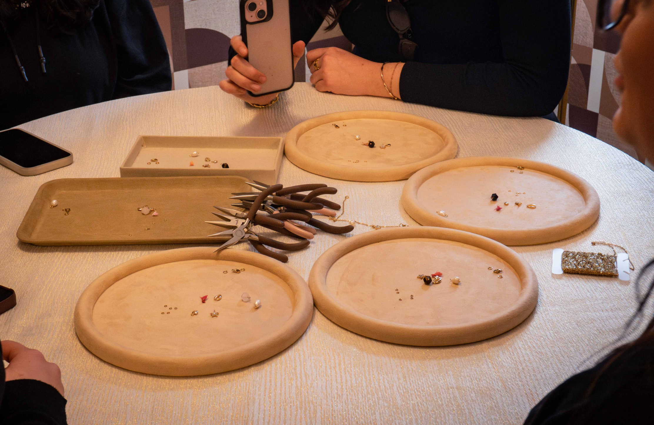 A workshop table is prepared with trays, beads, and jewelry tools. The participants create their creations in a calm and creative atmosphere.