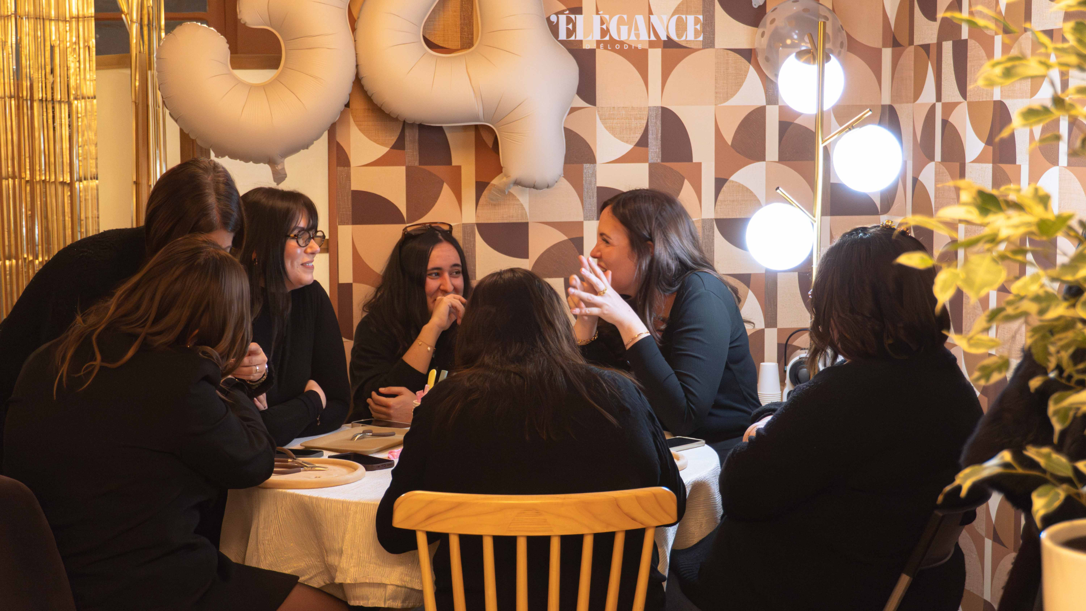 A group of women is gathered around a table in a warm and intimate atmosphere. They discuss and participate in a creative jewelry workshop under a soft light, with a friendly and relaxed atmosphere.