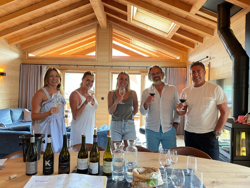 A group of five participants take part in a wine tasting workshop in a bright chalet. Glasses in hand, they discover different cuvees in a friendly and warm atmosphere, guided by an educational and sensory approach to wine.
