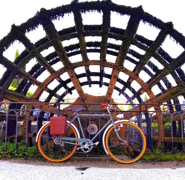 An antique black city bike is photographed in front of a paddle wheel, a symbol of the heritage of L.