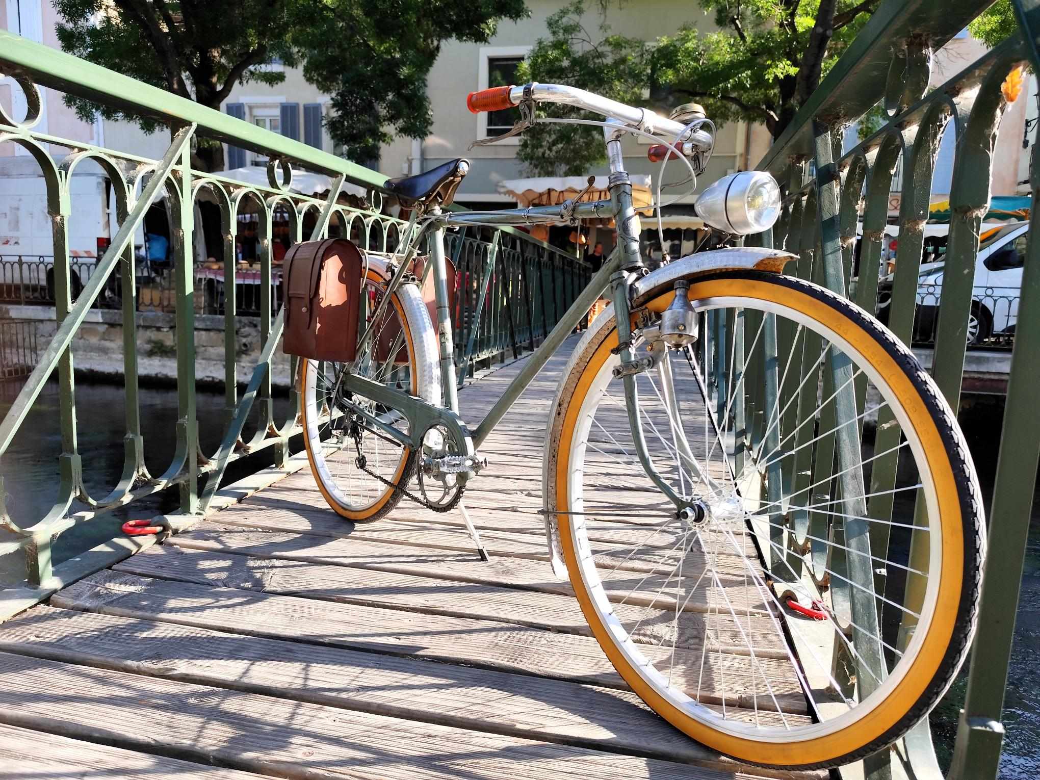 A vintage bike is photographed on a metal footbridge crossing the Sorgue. The decor highlights the city