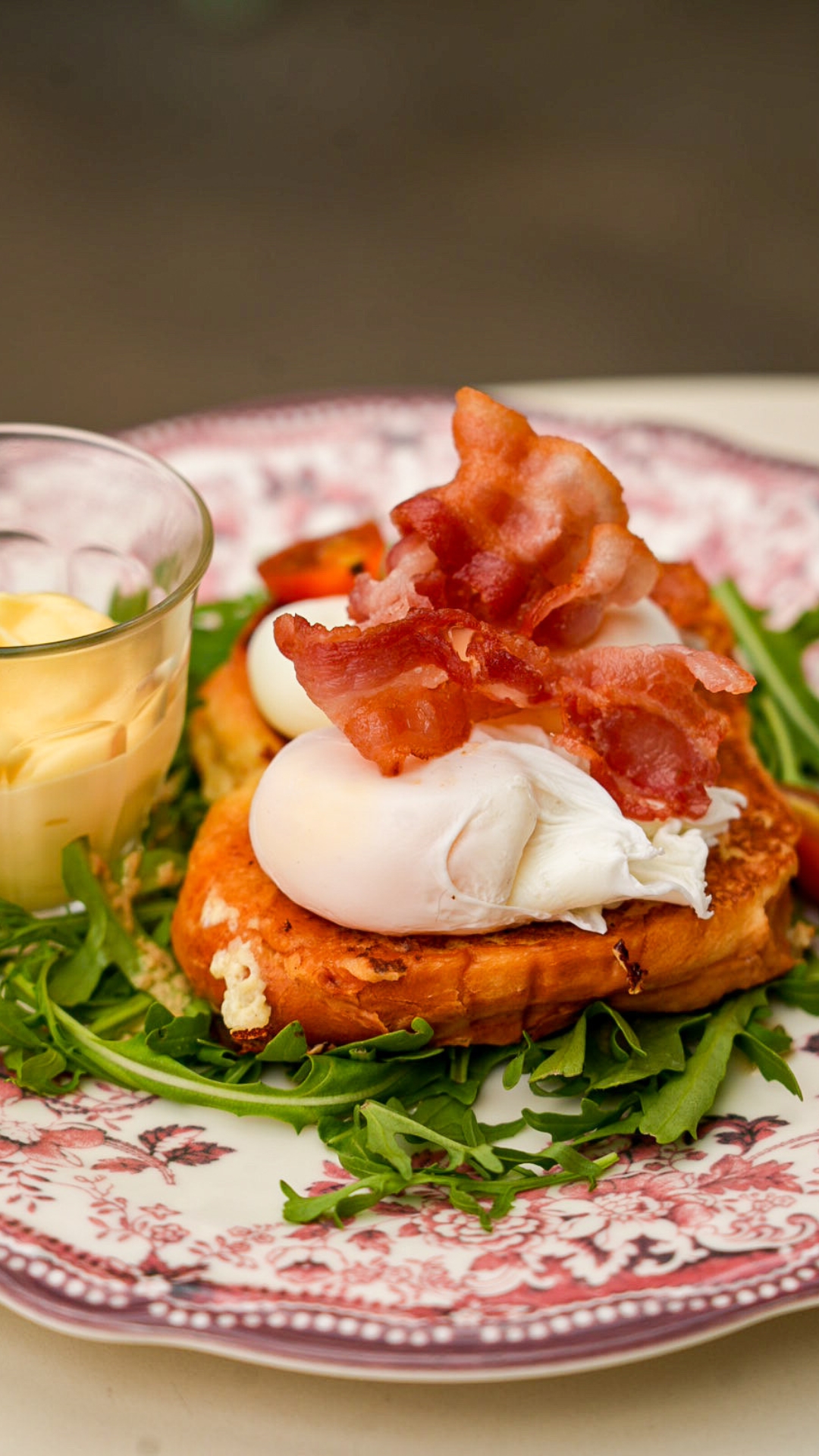 A generous slice of golden brioche welcomes two poached eggs with a melting heart, delicately topped with slices of crispy bacon. L
