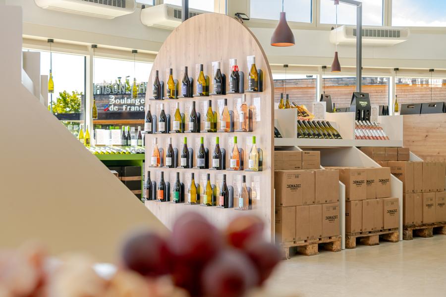 Interior view of the Demazet cellar, bright and contemporary, with a wide selection of wine bottles presented on wooden shelves. The space highlights the different wines of the cellar in a modern and welcoming atmosphere.